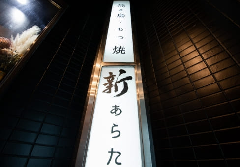 「焼き鳥・もつ焼き 新（あらた）」と書かれた縦型の看板